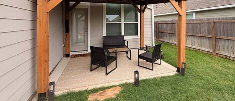 A covered patio with two chairs and a table, a wooden pergola, and a grassy yard.