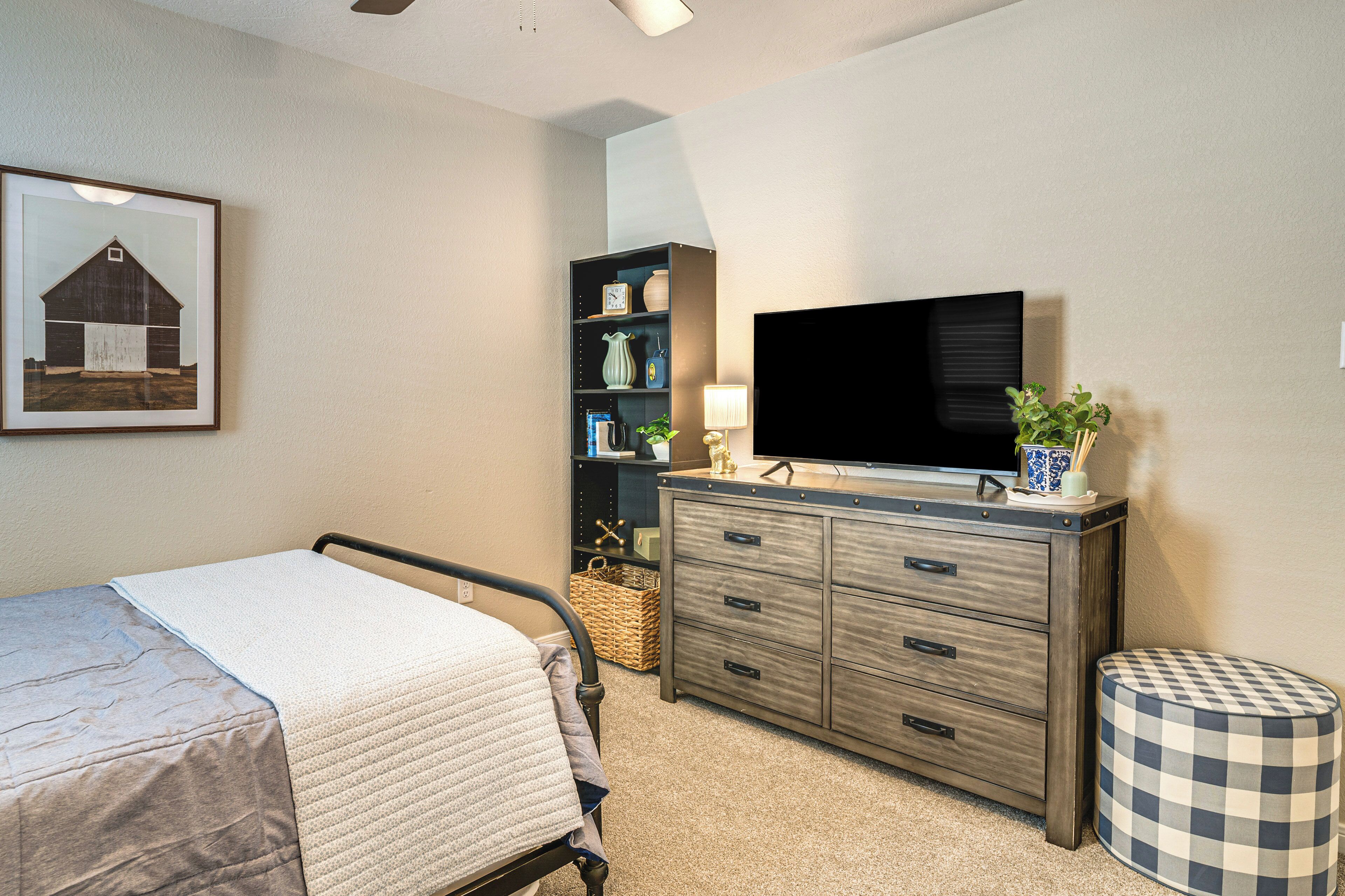 Un dormitorio con cama, cómoda, televisor y un cuadro en la pared.