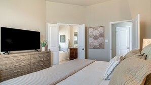 A bedroom with a large bed, a flat-screen TV on a wooden dresser, and a bathroom visible through an open door.