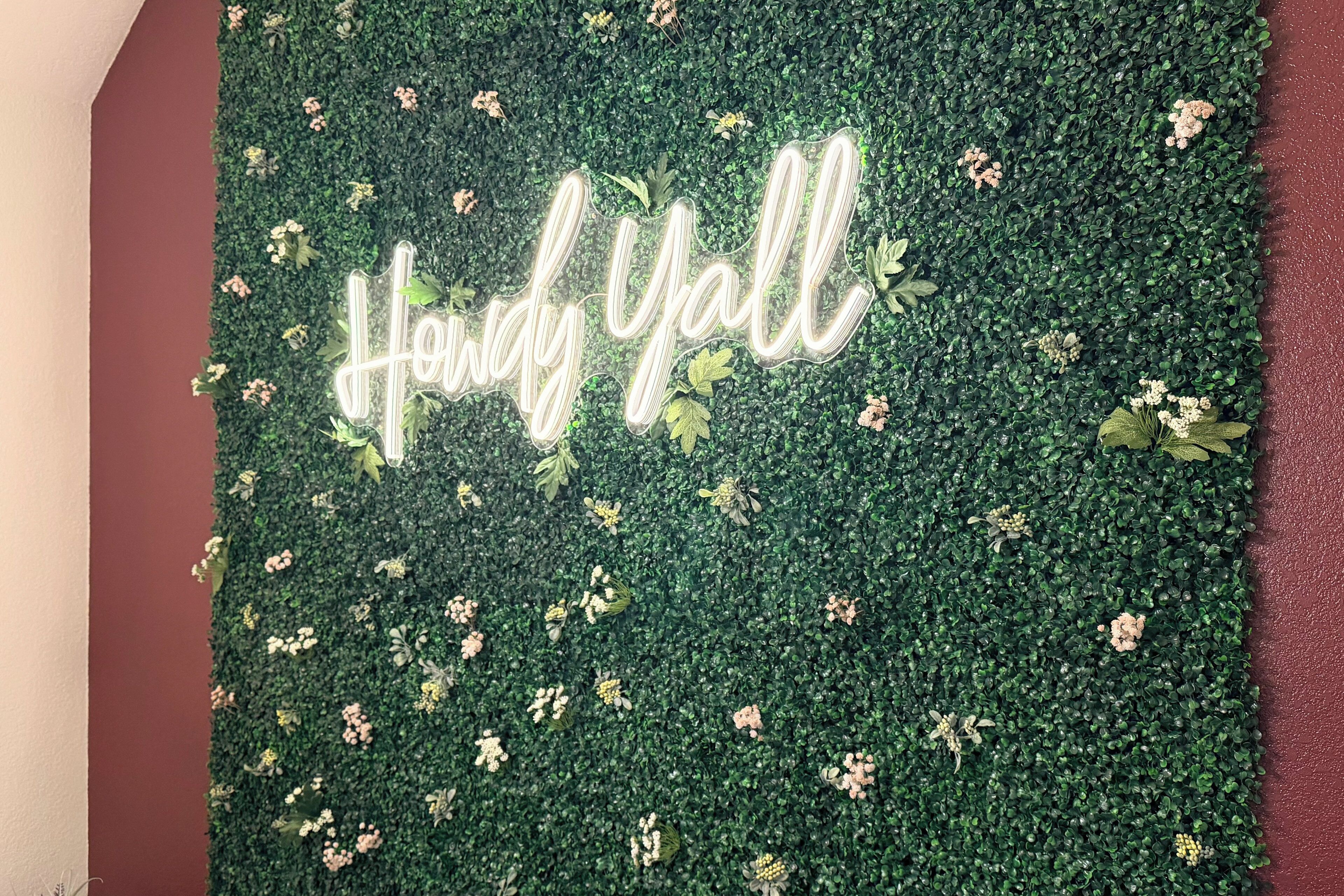 A wall with a green textured backdrop and the phrase 'Handy Yall' in illuminated letters.