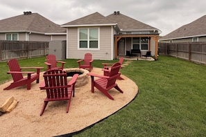 Un jardin avec un foyer entouré de fauteuils Adirondack, une terrasse en bois et un patio couvert.