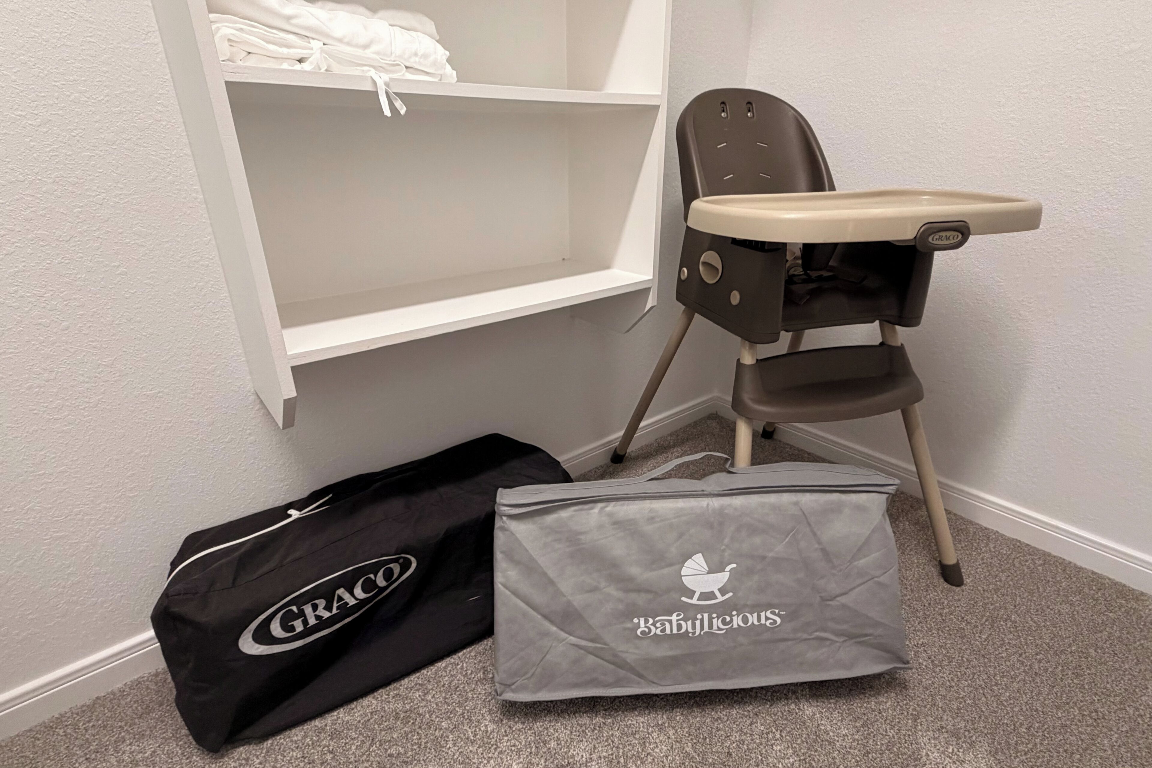 A baby changing station with a high chair and a storage bag labeled 'GRACO' and 'Babylicious'.