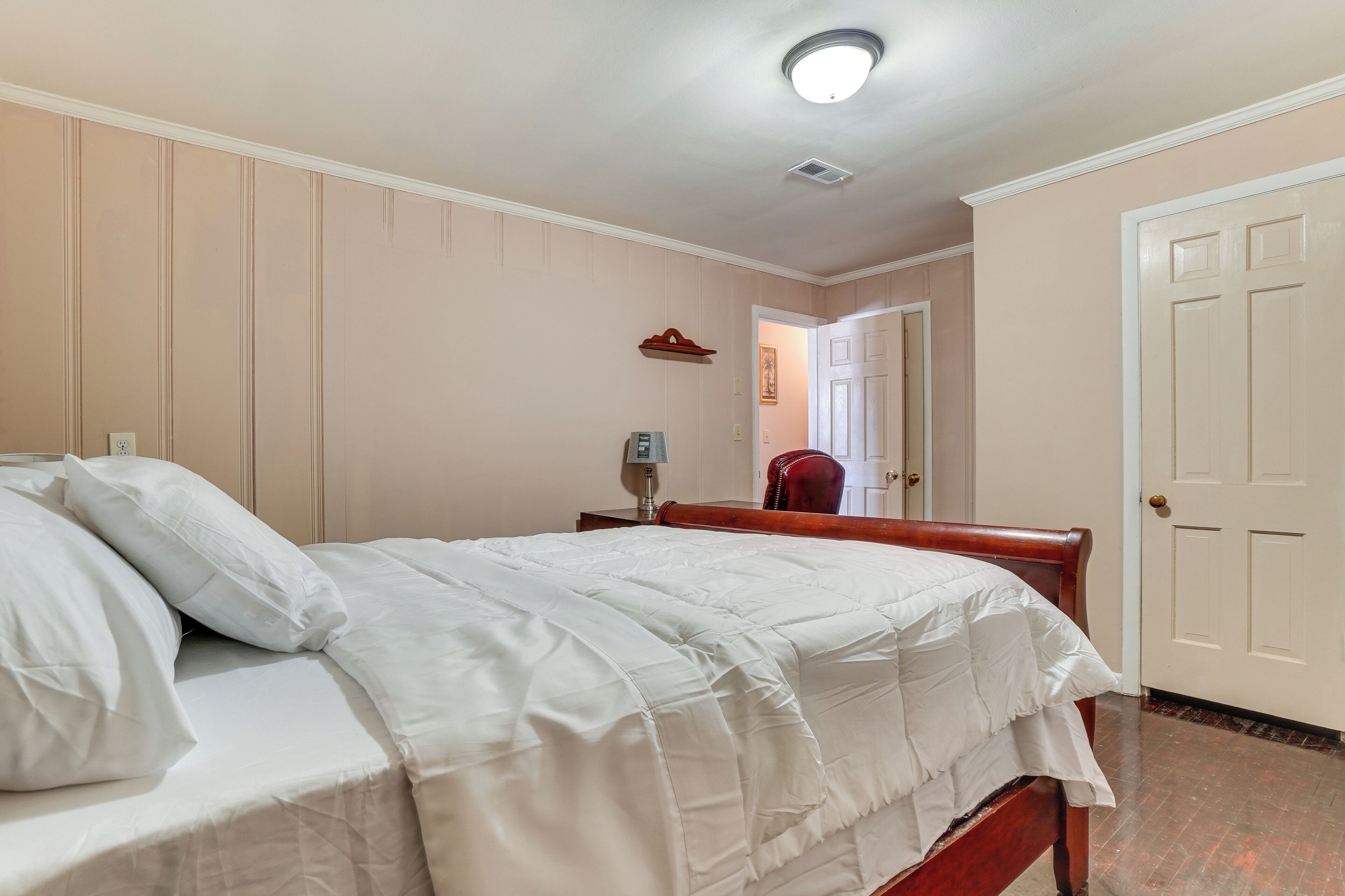 Een slaapkamer met een bed, nachtkastje, lamp en een deur.