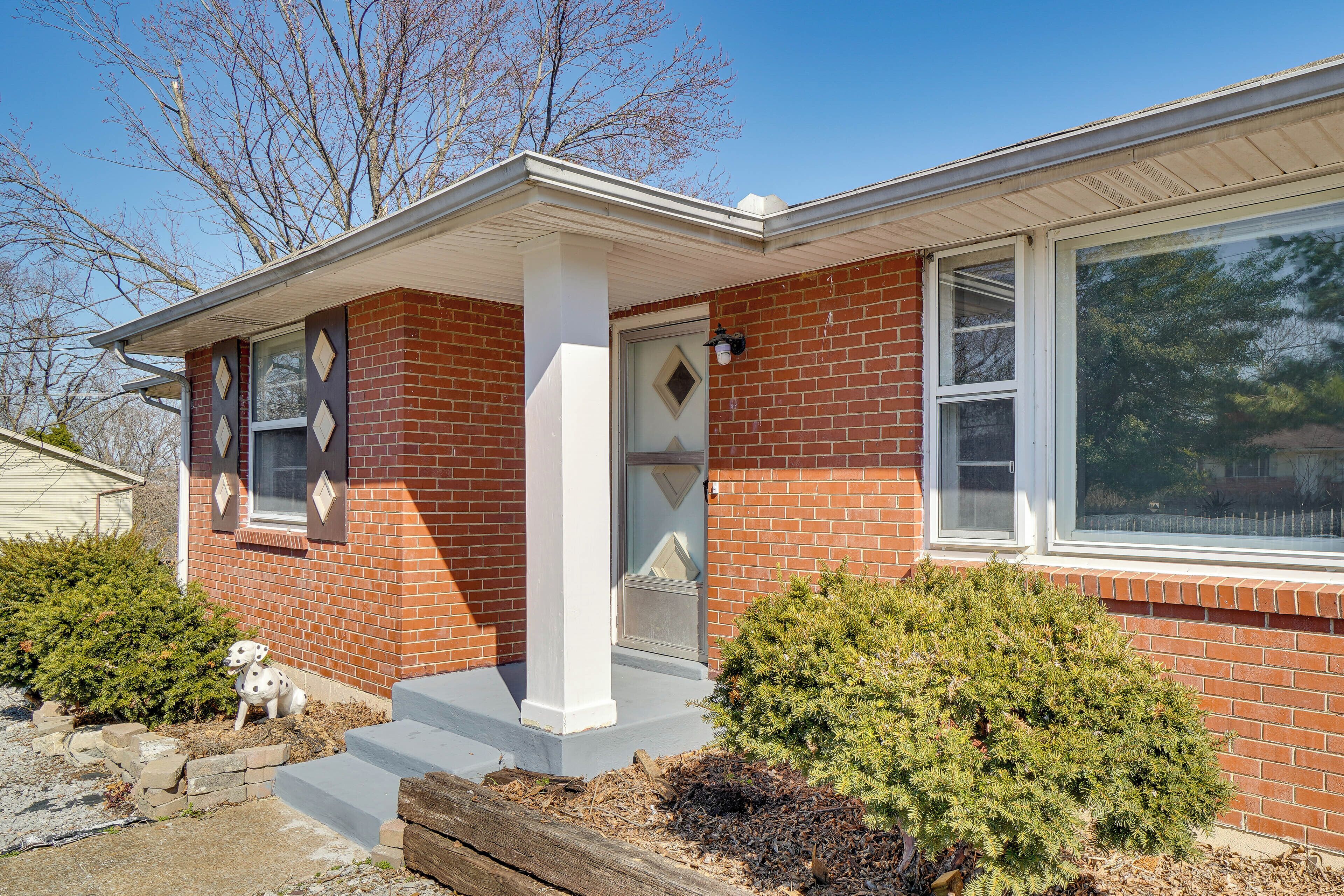 A brick house with a white porch, a small dog statue, and a well-maintained front yard.