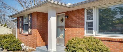 A brick house with a white porch, a small dog statue, and a well-maintained front yard.