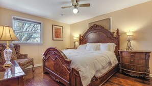 Un dormitorio con una cama de madera, una mesita de noche, una silla, una lámpara y un ventilador de techo.