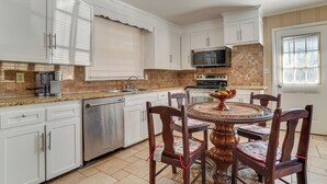 Una cocina con armarios blancos, microondas, lavavajillas y una mesa de comedor con sillas.