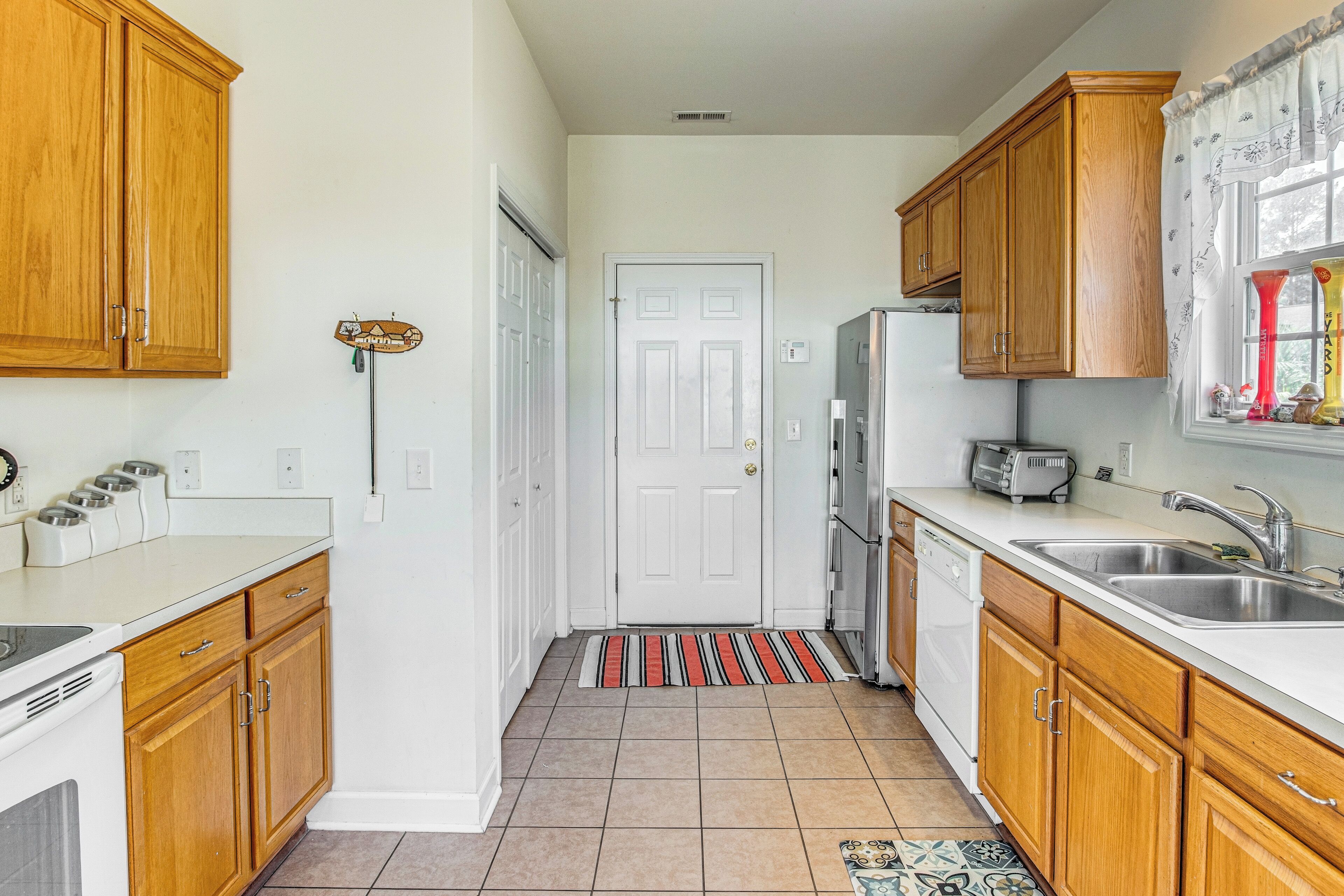 A kitchen with wooden cabinets, a white countertop, a stainless steel sink, and a refrigerator.