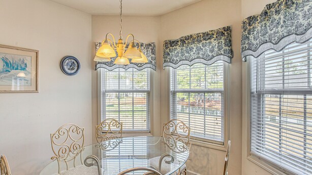 A dining area with a glass table and ornate chairs, large windows with blinds, and a chandelier. - Pool Access & Pond Views: Longs Home Near Golf! (Longs)