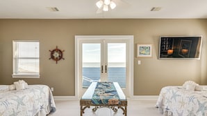 Ein Schlafzimmer mit einem großen Fenster, einem Bett mit sternfischigem Überwurf, einem Tisch mit Tischläufer mit Seestern-Muster, einer Schiffslenken-Wanddekoration und einem gerahmten Bild an der Wand.