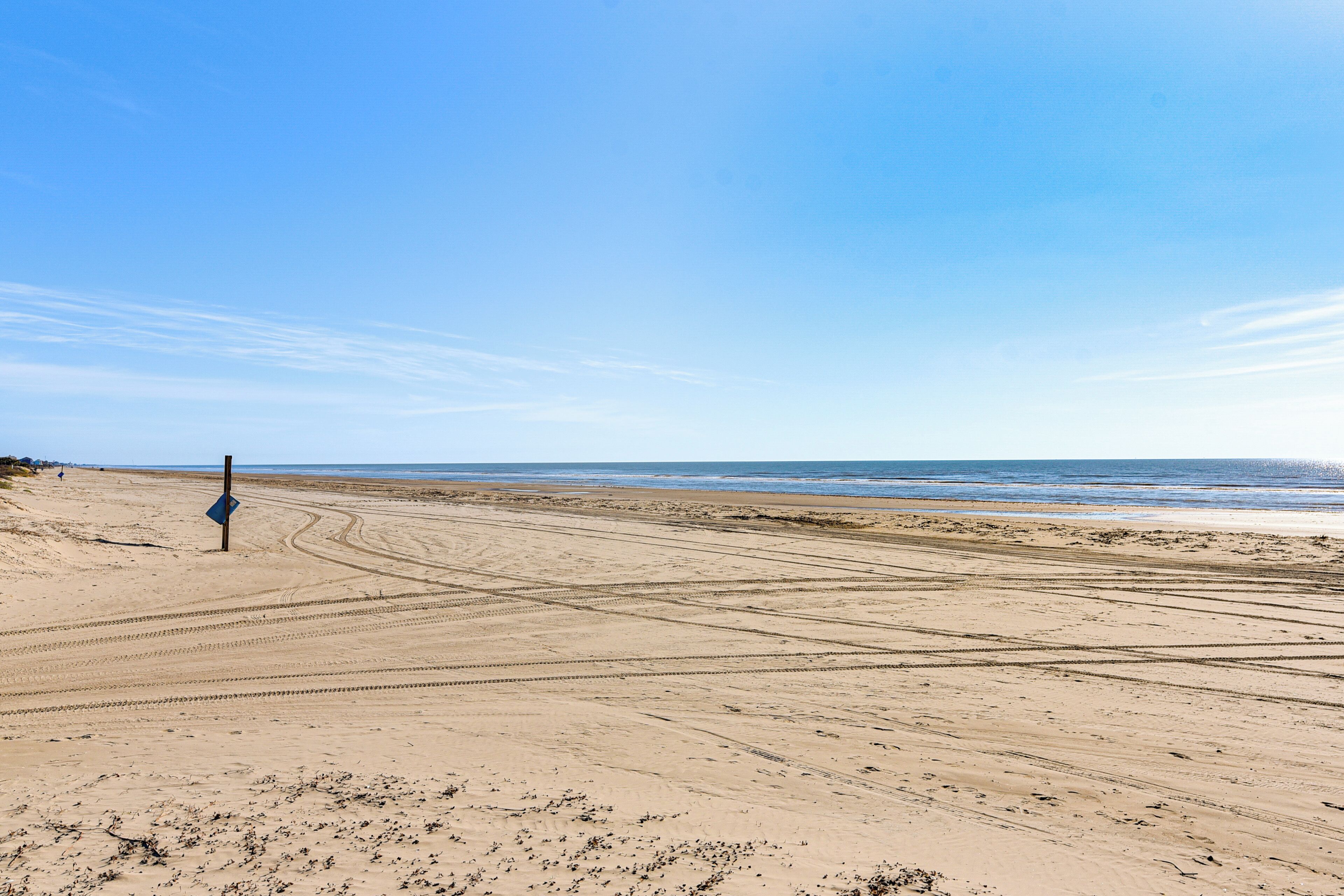 A wide sandy beach with tire tracks and a blue sign.
