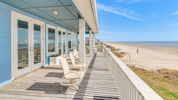 Ein Gebäude direkt am Strand mit einer Holzterrasse, Sitzmöglichkeiten im Freien und Blick auf den Strand.