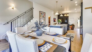 A modern kitchen with a central island, a dining area with a long table, and a staircase leading to another level. - Designer Wheeler Retreat: Walk to Dining! (Oklahoma City)