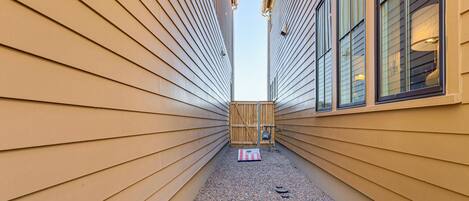 A narrow pathway with wooden siding walls and a gravel path leading to a wooden gate.