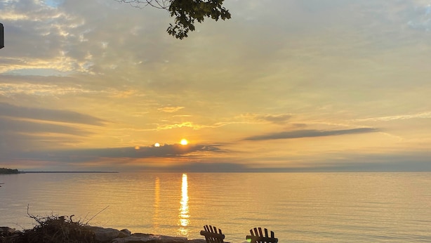 A sunset over a calm body of water with two Adirondack chairs facing the water. - Waterfront Cottage: Family Getaway at Lake Huron! (East Tawas)