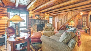 A cozy log cabin interior with a fireplace, wooden furniture, and a staircase. - Waterfront Cottage: Family Getaway at Lake Huron! (East Tawas)