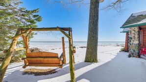 A wooden swing chair in a snowy area with a view of the ocean. - Waterfront Cottage: Family Getaway at Lake Huron! (East Tawas)