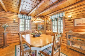 Interior de una cabaña de madera con una mesa de comedor, sillas, una lámpara de araña y una estantería.