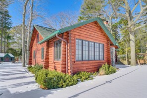 Una cabaña de troncos con techo verde, rodeada de nieve y árboles.