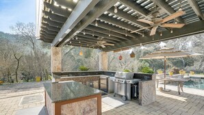 An outdoor kitchen area with a stone countertop, built-in grill, and ceiling fans. - Pool, Peacocks & Views! Lavish Retreat in Gilroy (Gilroy)