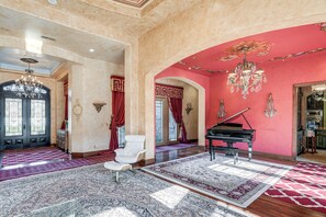 A grand room with a piano, a white armchair, and a large chandelier.