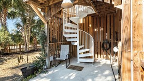 A wooden spiral staircase leading to an upper level, a white chair, and a hanging light fixture. - Elevated Pet-Friendly Retreat Near the Beach (Tybee Island)
