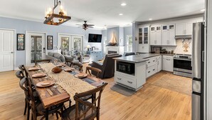 A spacious kitchen with modern appliances, a dining area with a wooden table and chairs, and a living room with a sofa and television. - Elevated Pet-Friendly Retreat Near the Beach (Tybee Island)