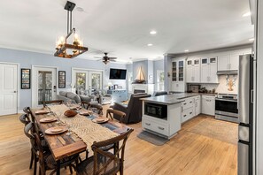 A spacious kitchen with modern appliances, a dining area with a wooden table and chairs, and a living room with a sofa and television. - Elevated Pet-Friendly Retreat Near the Beach (Tybee Island)