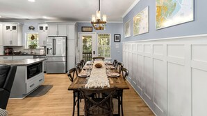 A modern kitchen with white cabinetry, stainless steel appliances, and a wooden dining table with a decorative runner. - Elevated Pet-Friendly Retreat Near the Beach (Tybee Island)