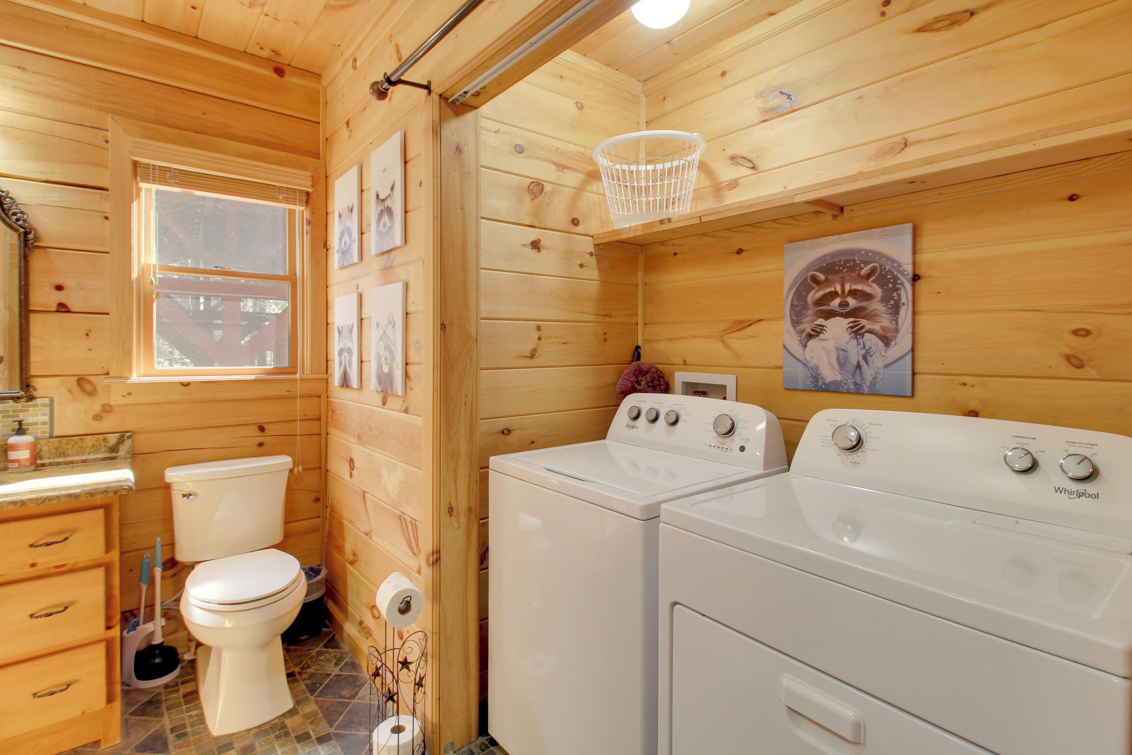 A wooden cabin bathroom with a toilet, sink, and two white Whirlpool washers.