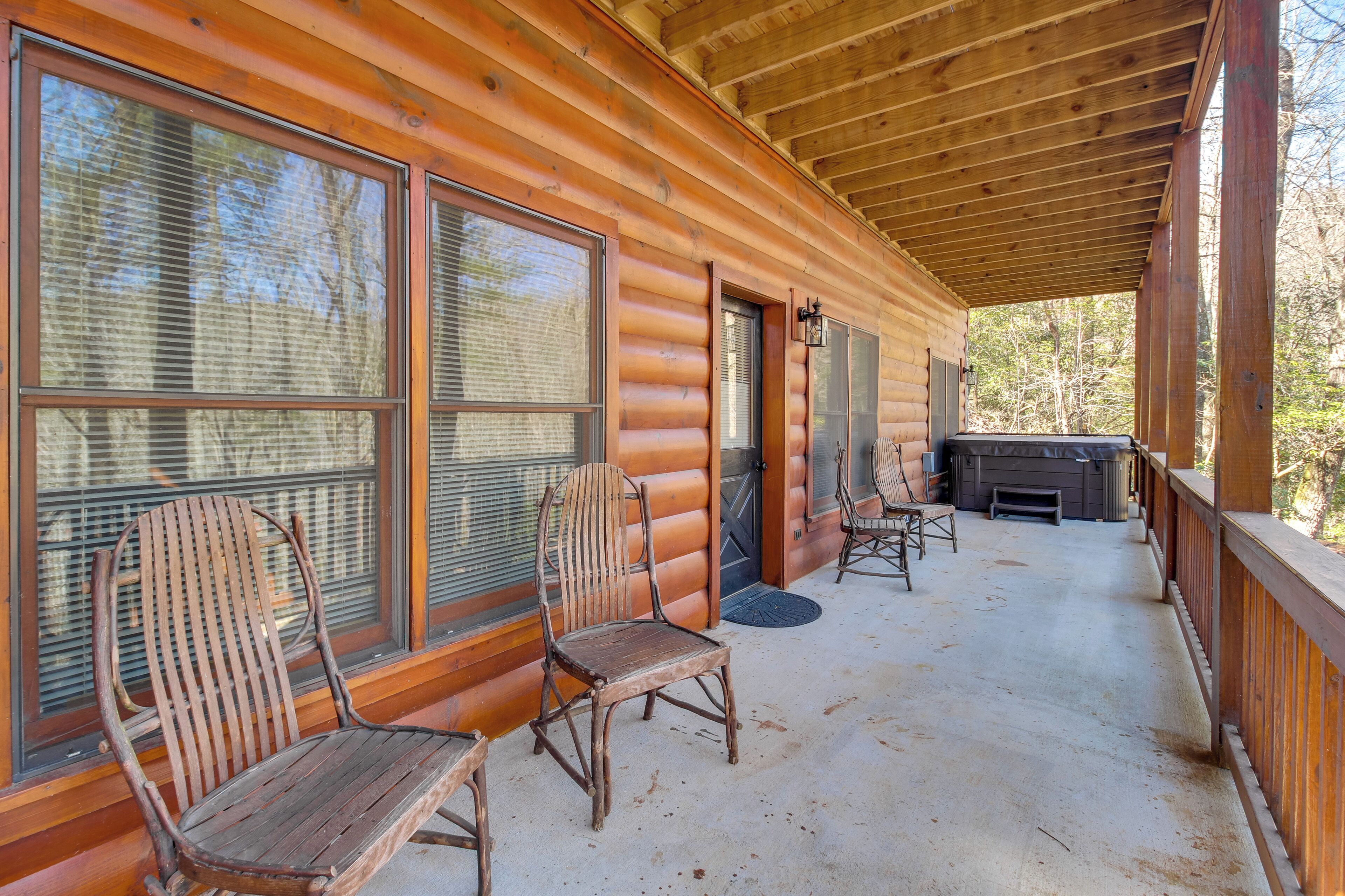 Eine Holzhütte mit überdachter Veranda, zwei Holzstühlen, einem Kamin und einem großen Fenster.