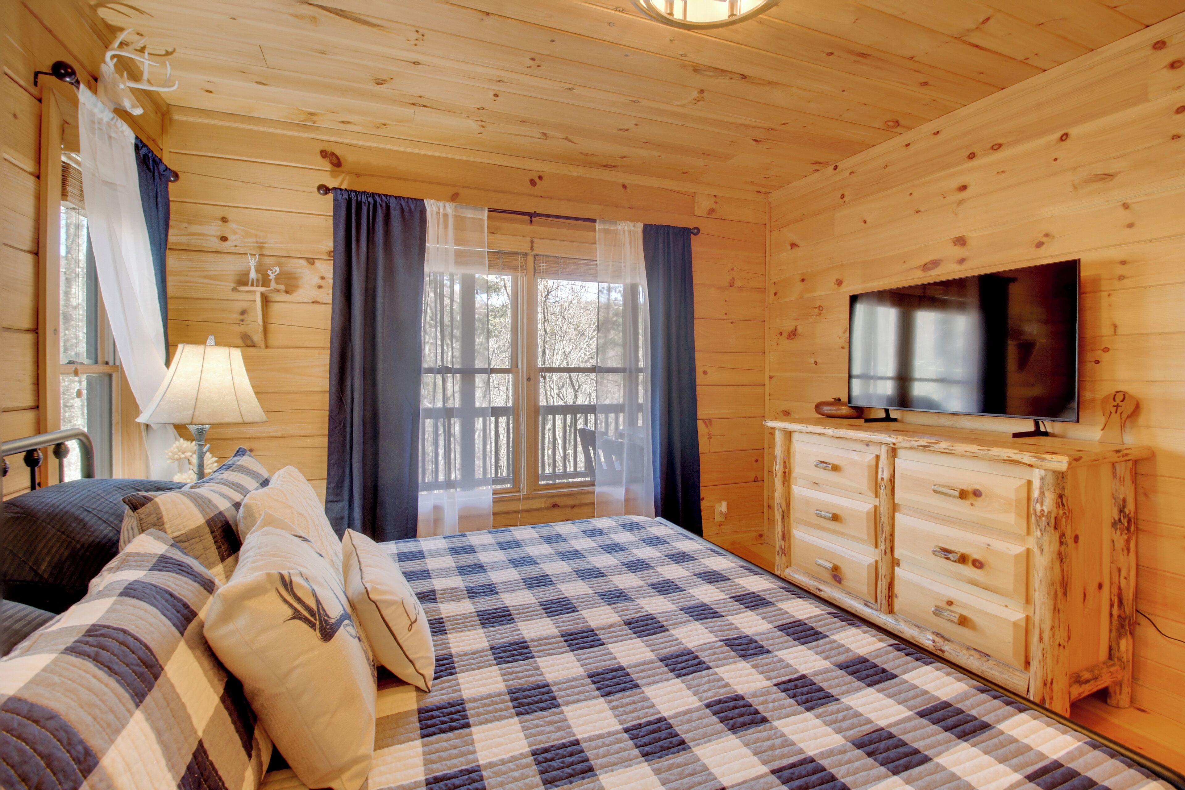 A cozy cabin room with a checkered bed, a television, and a wooden cabinet.