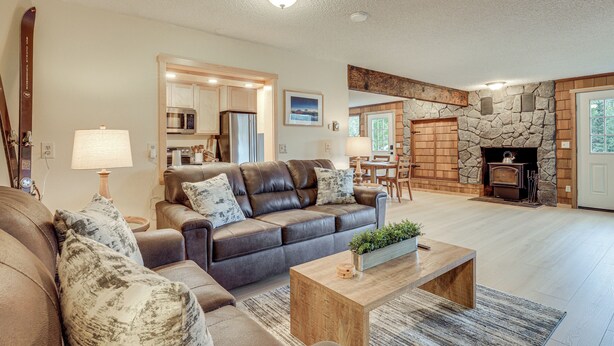 A spacious living room with a leather sofa, wooden coffee table, and a stone fireplace. - Après & Adventure: Mt Hood Retreat in Gov Camp! (Government Camp)