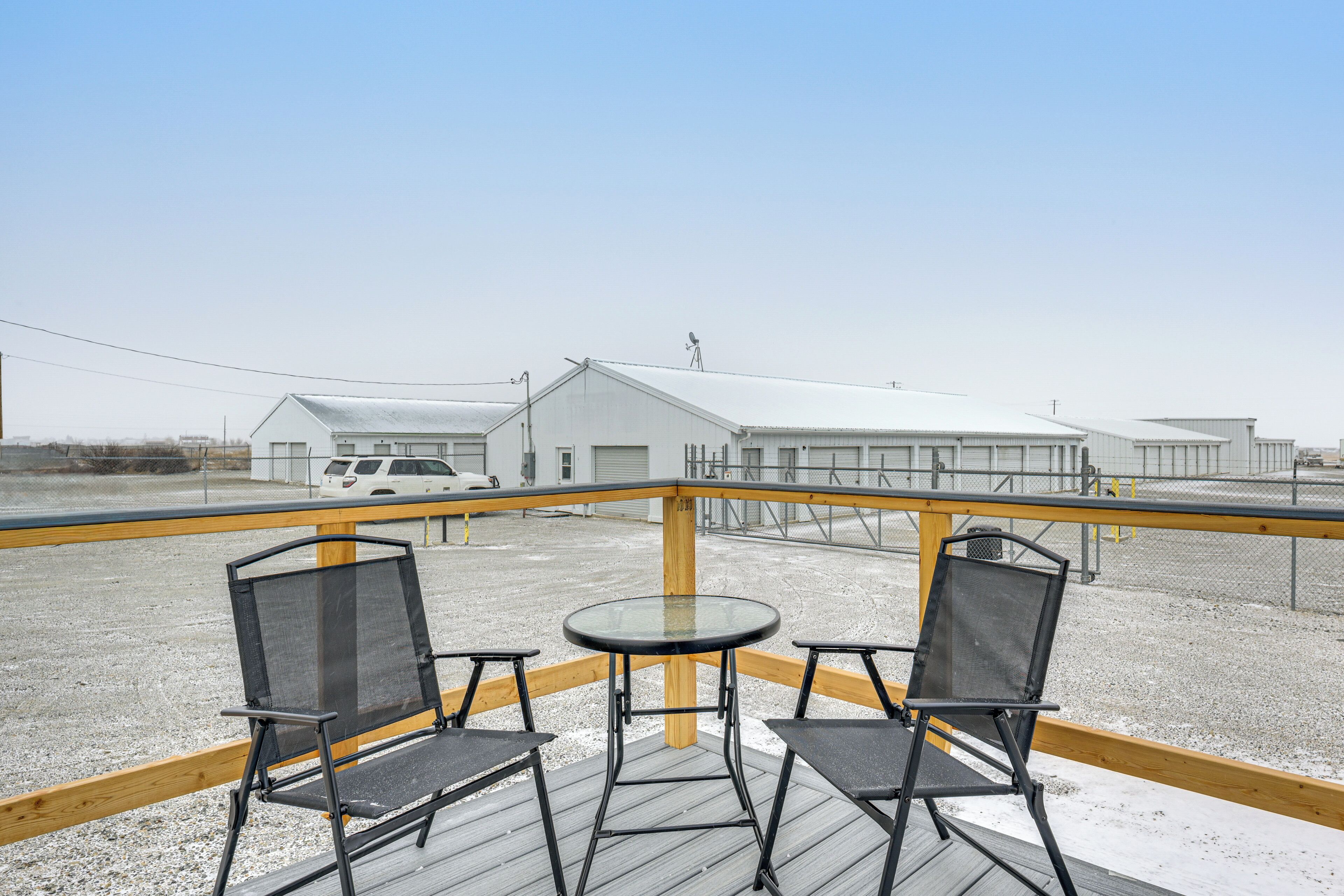 A balcony with two chairs and a table, overlooking a parking area and buildings.
