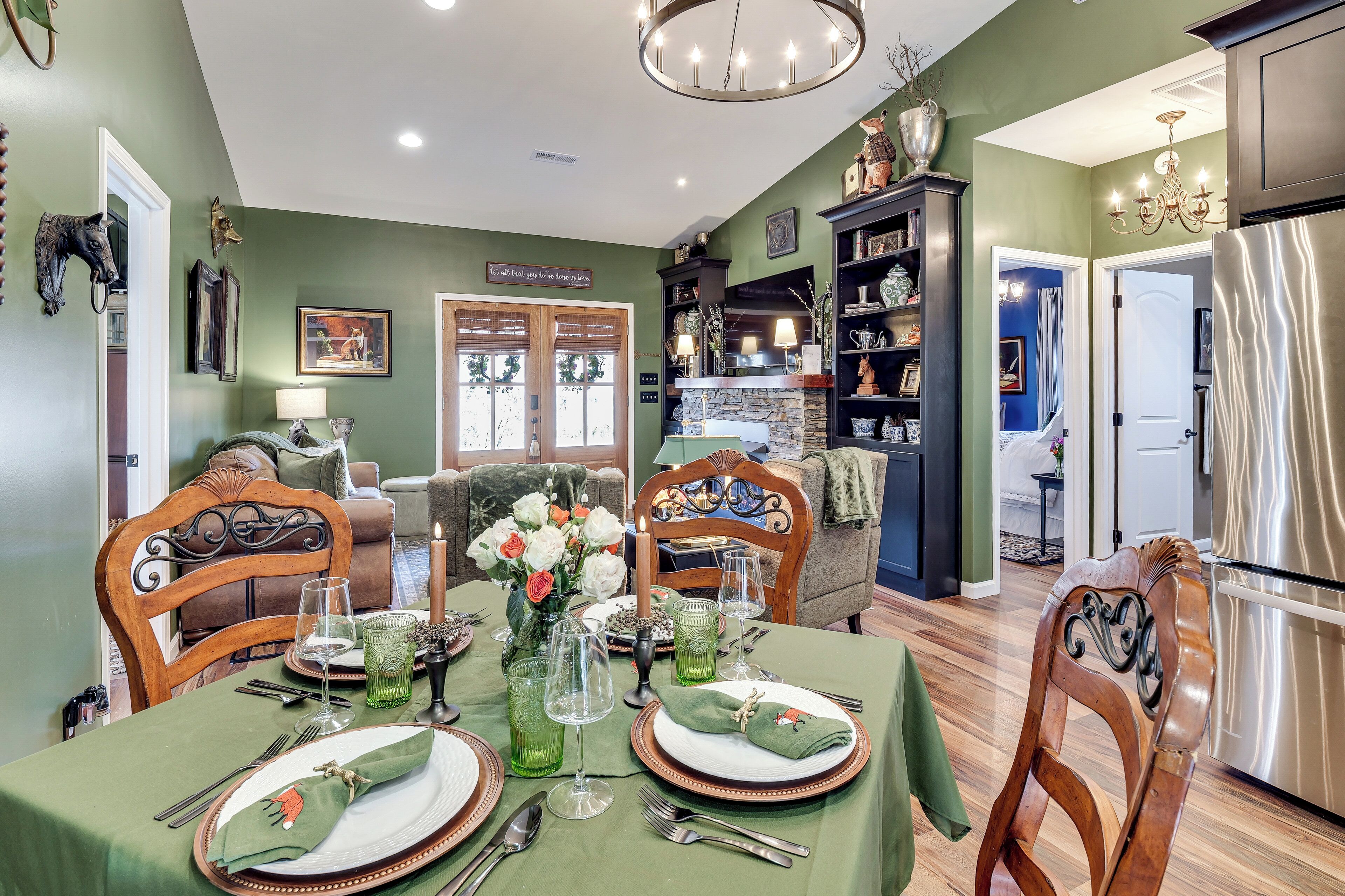 A dining area with a green table set for two, wooden chairs, and a chandelier.