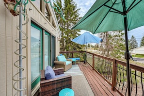 A deck with wicker furniture, a blue umbrella, and a railing.