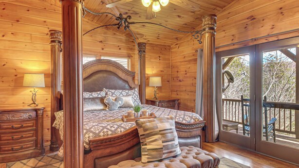 A wooden cabin bedroom with a large bed, a bench, and a balcony with a view of trees. - Hot Tub + Mtn Views: Peaceful Blue Ridge Retreat! (Blue Ridge)