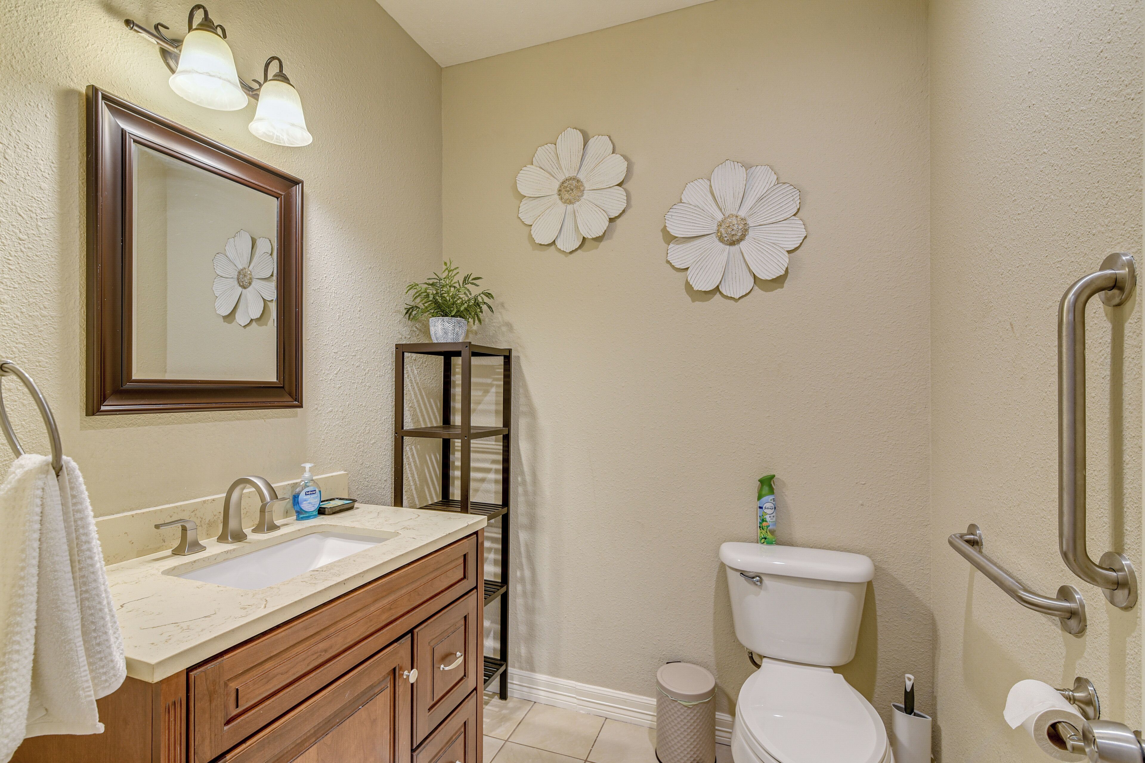 Une salle de bain équipée d’un lavabo, d’un miroir, de toilettes et de barres d’appui.