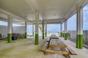 Un pabellón al aire libre con mesas y sillas de picnic, suelo de hormigón y vistas a la playa y al océano.