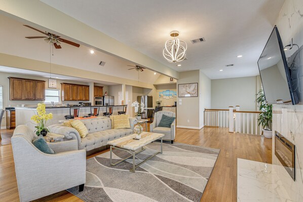 A spacious living area with a sofa, coffee table, and a ceiling fan. A kitchen is visible in the background. - Saltwater Pool! Epic Galveston Bay Group Getaway! (Dickinson)