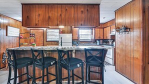 A kitchen with wooden cabinets, a central island with bar stools, and a microwave. - 2 Mi to MSU Campus! Family Abode w/ Spacious Yard (Starkville)