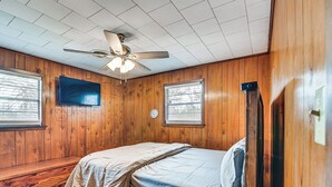 A bedroom with wooden walls, a ceiling fan, a bed with a white comforter, and two windows with blinds. - 2 Mi to MSU Campus! Family Abode w/ Spacious Yard (Starkville)