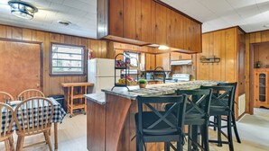 A kitchen with wooden cabinets, a central island with chairs, a refrigerator, and a window with blinds. - 2 Mi to MSU Campus! Family Abode w/ Spacious Yard (Starkville)