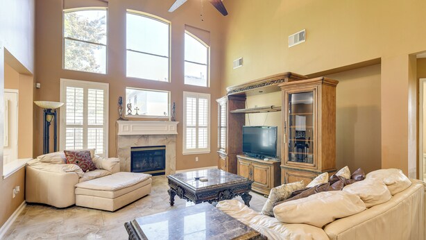 A spacious living room with a high ceiling, large windows, a fireplace, a television, and a wooden cabinet. - 3,500-sq-ft Retreat w/ Private Yard in Sugar Land! (Sugar Land)