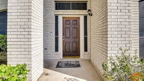 A white brick building with a wooden door, a small window above the door, and a doormat on the ground. - 3,500-sq-ft Retreat w/ Private Yard in Sugar Land! (Sugar Land)
