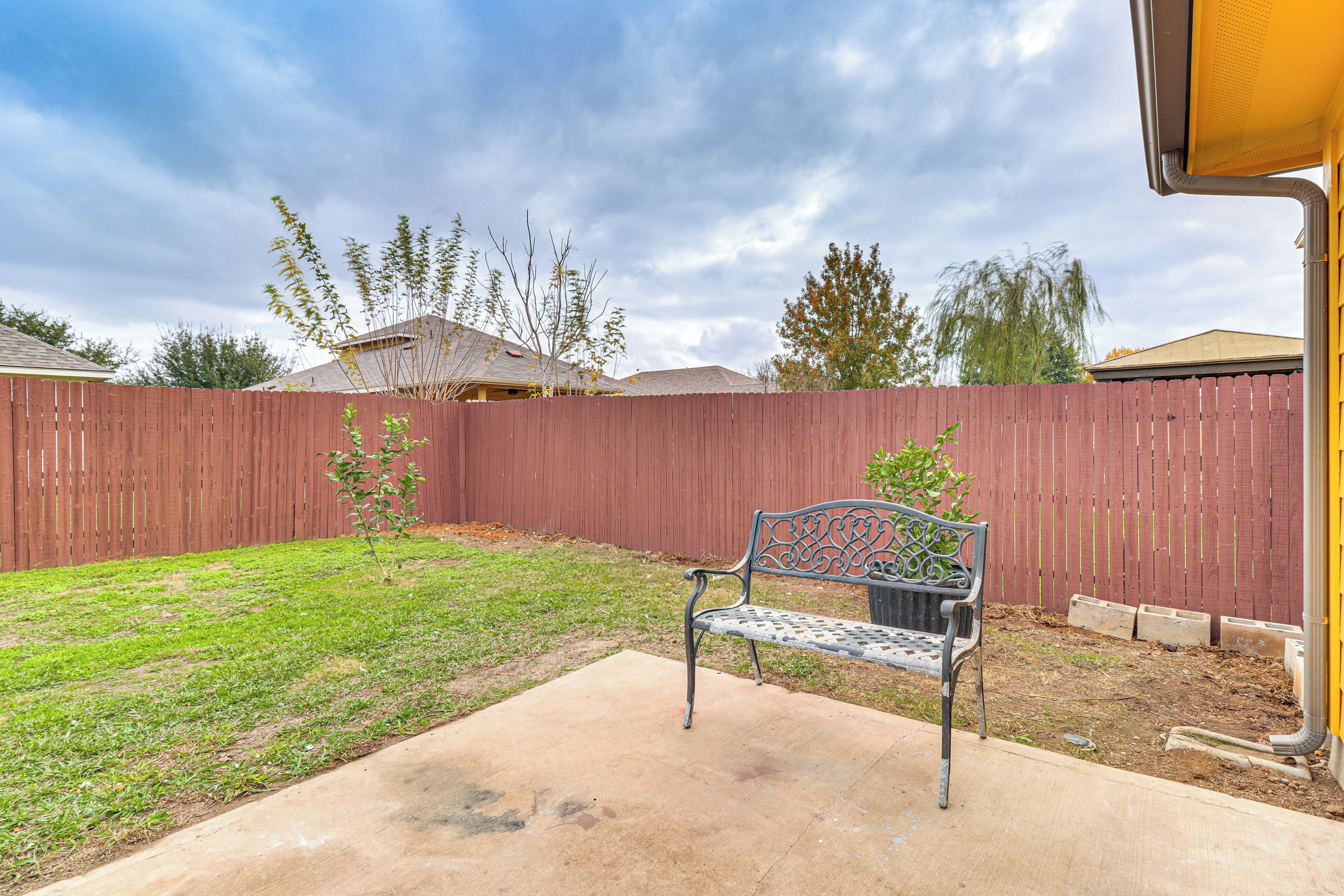 A backyard with a wooden fence, a metal bench, and a concrete patio.