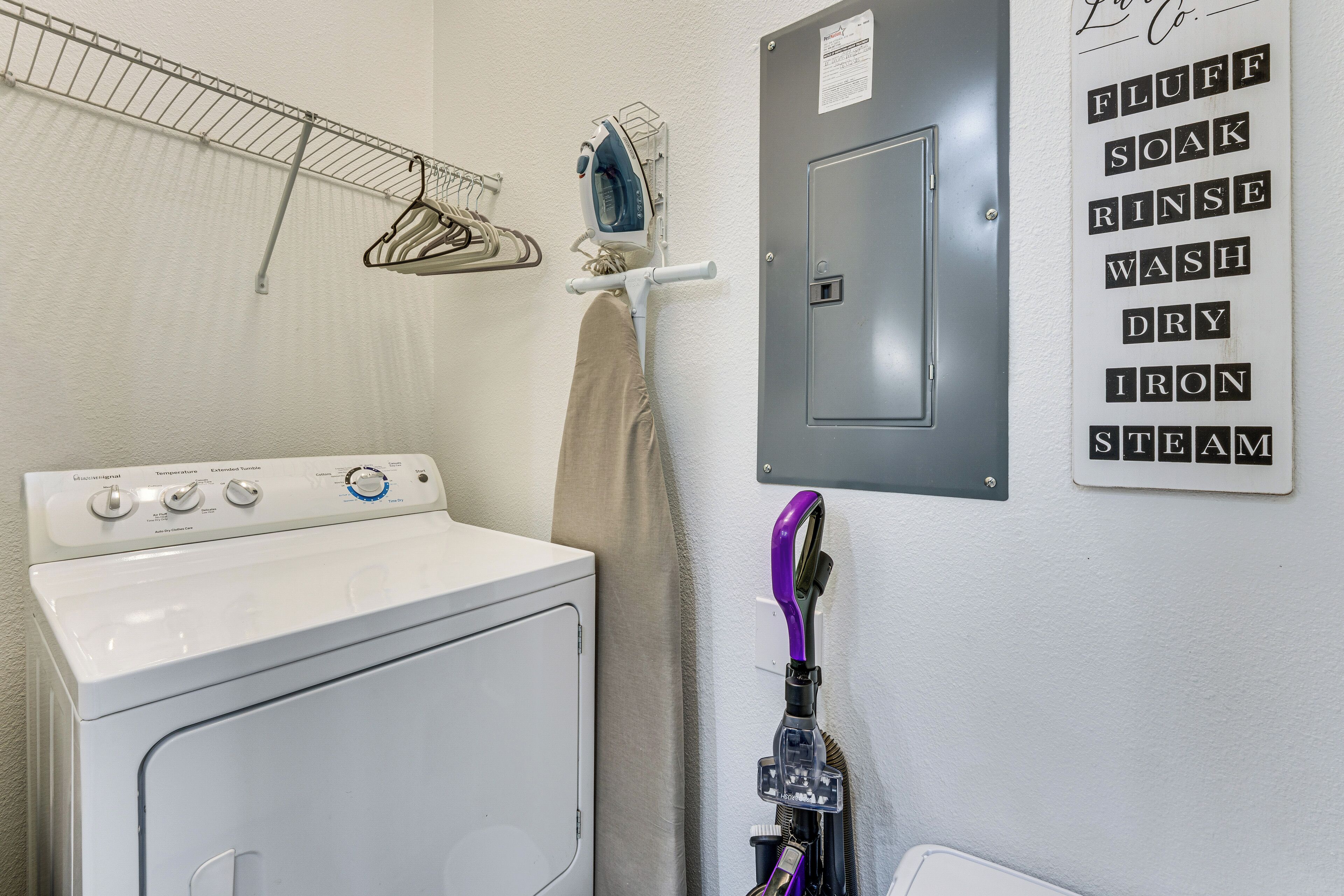 A laundry area with a washing machine, a drying rack, and a wall-mounted sign listing laundry steps.