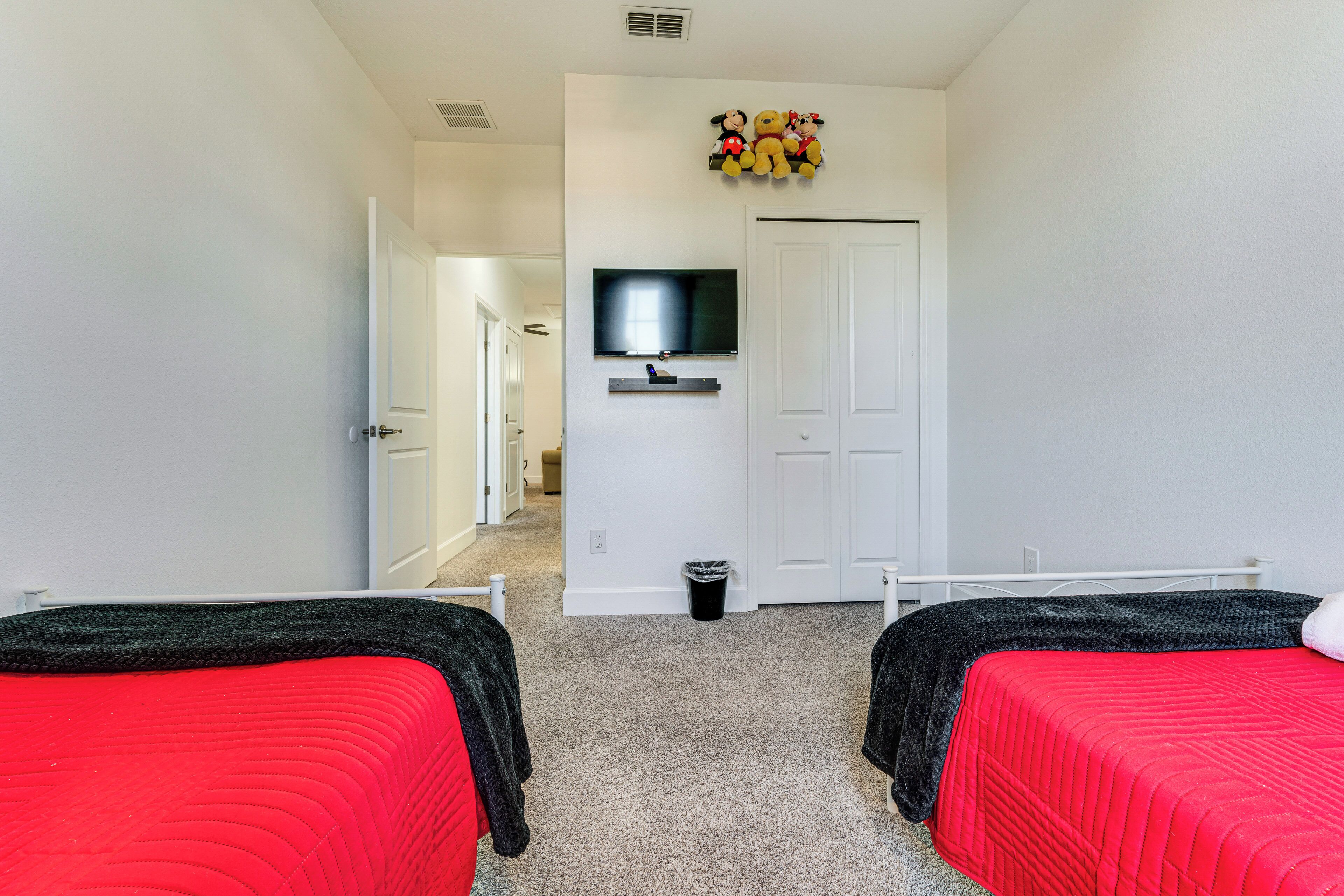 A hotel room with two single beds, a television mounted on the wall, and a trash bin.