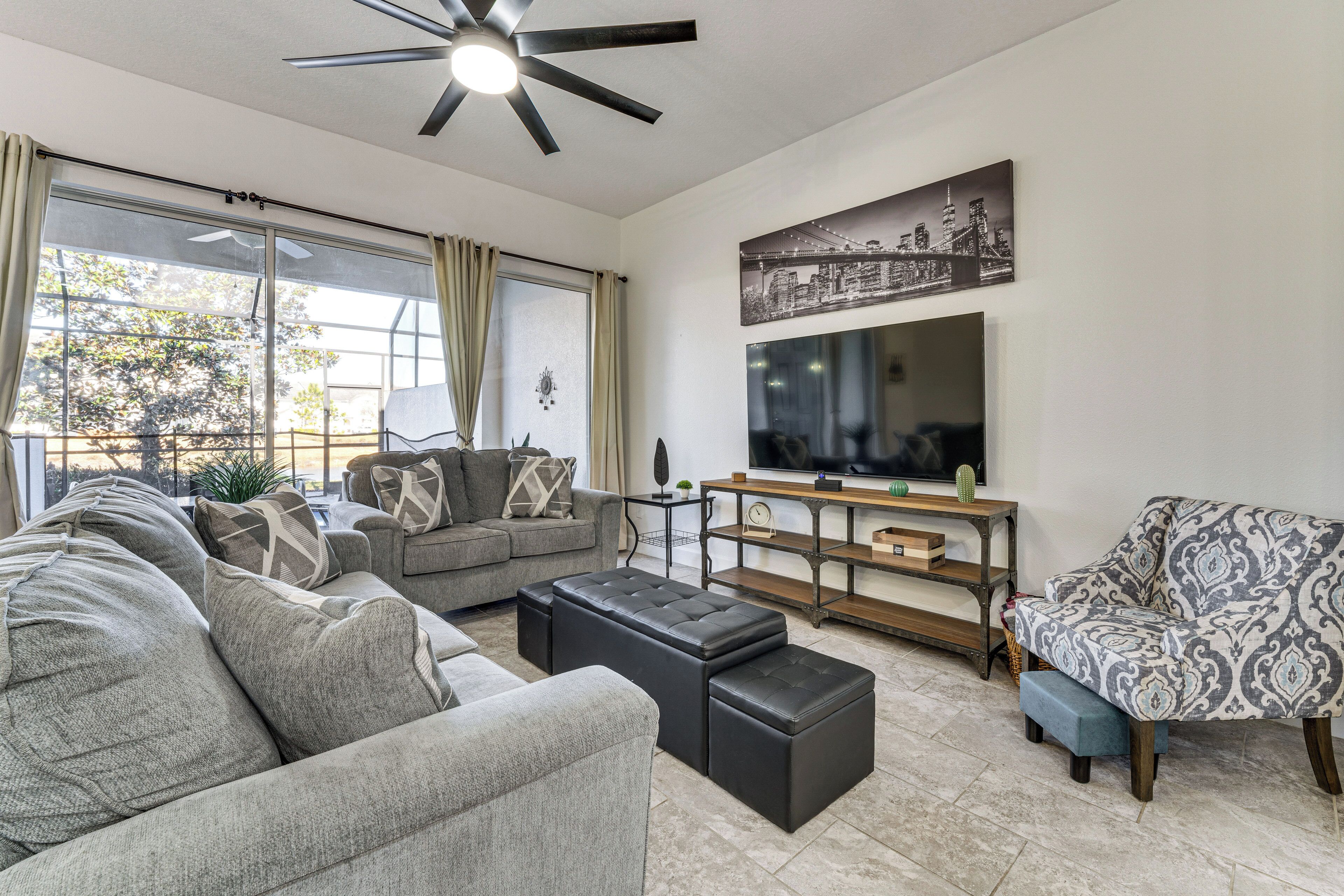 A modern living room with a sofa set, ottomans, a television, and a cityscape artwork on the wall.