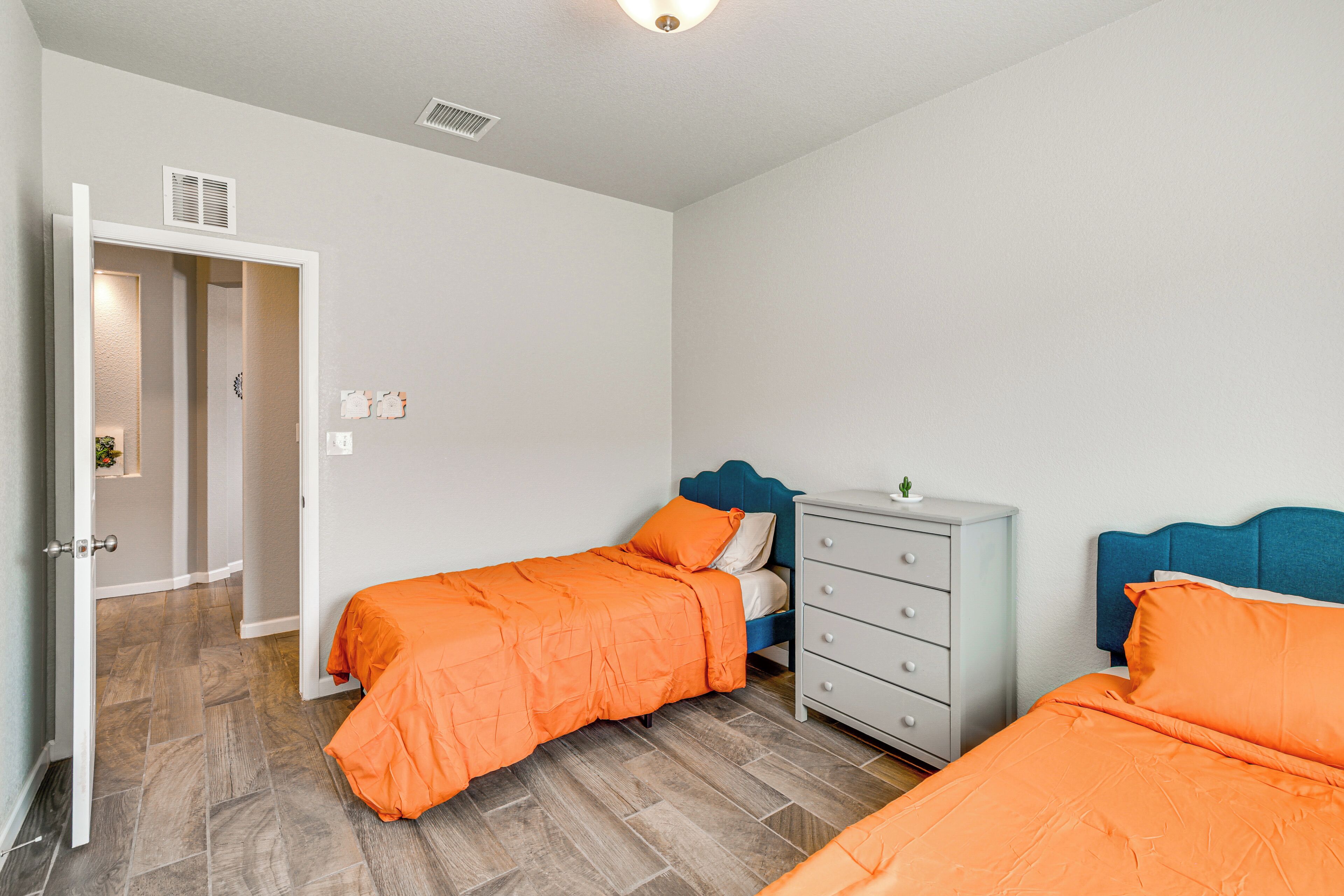A bedroom with two beds, a dresser, and a door leading to another room.